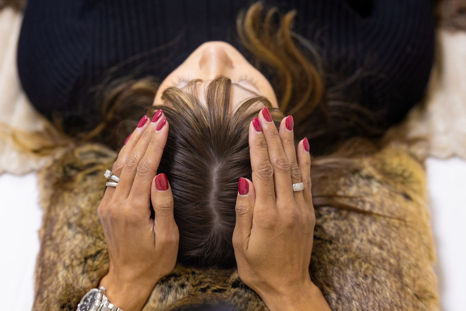 Person with red nails massaging another person's scalp, who is lying down with eyes closed.
